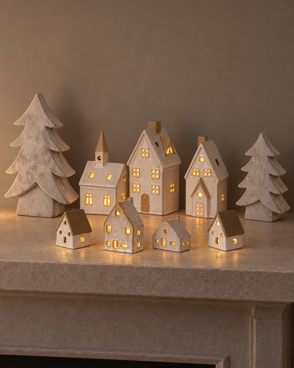 A white ceramic Christmas village glowing along a modern mantel