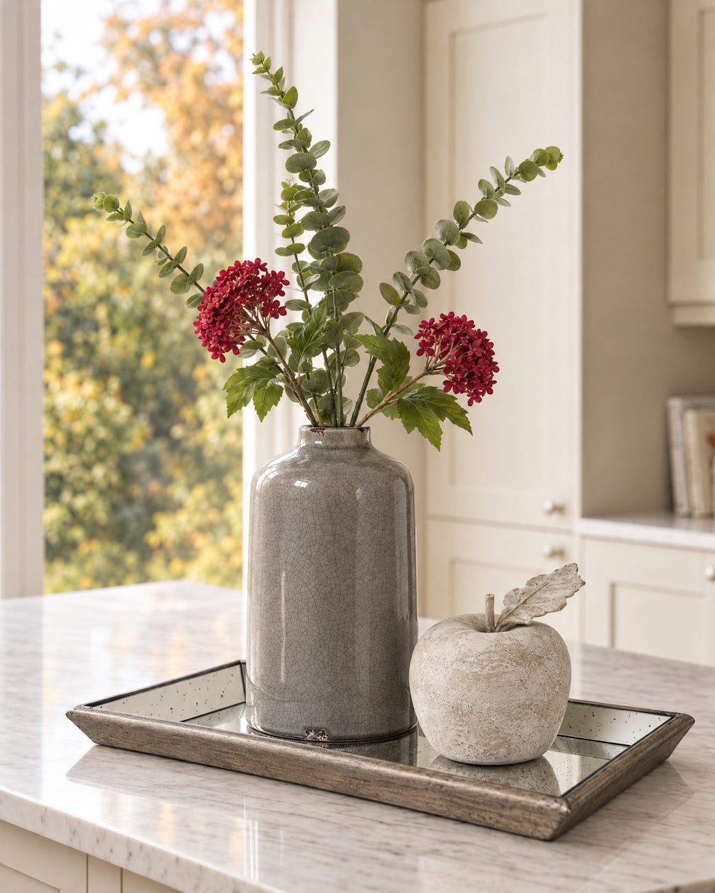 The Liv Tray Set on a marble kitchen island: Garda grey glazed vase with artificial gunnii eucalyptus and red viburnum, a stone apple and the Astor mirrored tray