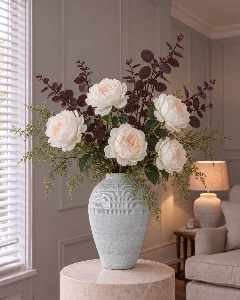 The Aurelia Blush Bouquet: five artificial blush garden roses, burgundy eucalyptus and feathery asparagus fern in the pale celadon Kemi Medium Olpe Vase from the With vase option, on a stone plinth in a panelled living room