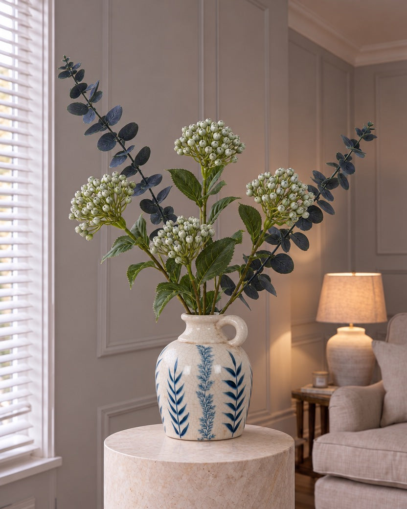 The Blue Flora Hydrangea Arrangement: artificial blue budding hydrangea sprays and dark eucalyptus in the Blue Flora Amphora Jug Vase on a stone plinth in a panelled living room