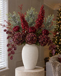 The Bordeaux Christmas Statement: artificial burgundy hydrangeas, peony roses, red spear hydrangeas, frosted pine and red berries in the textured white Ashen vase, on a stone plinth in a Christmas living room
