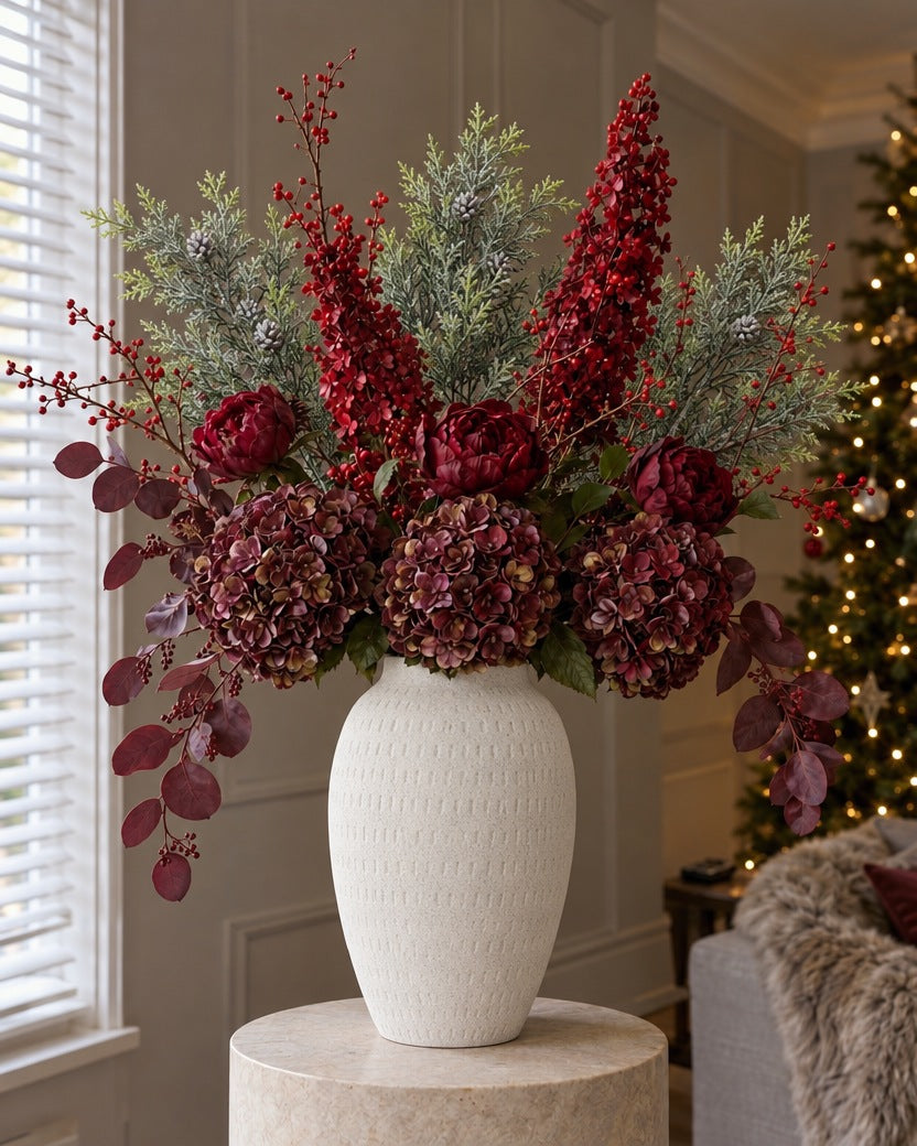The Bordeaux Christmas Statement: artificial burgundy hydrangeas, peony roses, red spear hydrangeas, frosted pine and red berries in the textured white Ashen vase, on a stone plinth in a Christmas living room