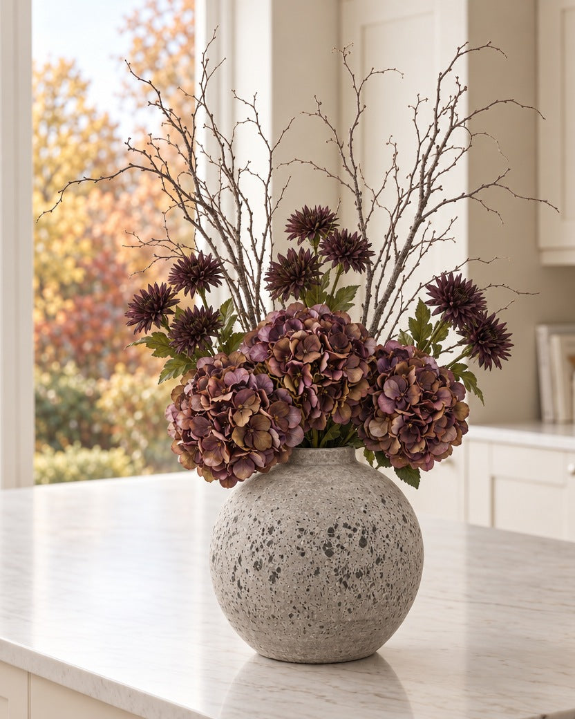 The Cocoa Autumn Bouquet: 3 artificial coffee hydrangeas, chocolate chrysanthemums and bare branch sprays, shown in the Tiber Stone Ceramic Vase (With vase option) on a kitchen island by an autumn window