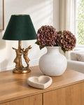 The Corner Edit: Antique Gold Marching Hares Lamp with green velvet shade, Darcy Squat Stone Vase with 2 artificial autumn coffee hydrangeas, and Deep Stone Heart Dish on an oak sideboard