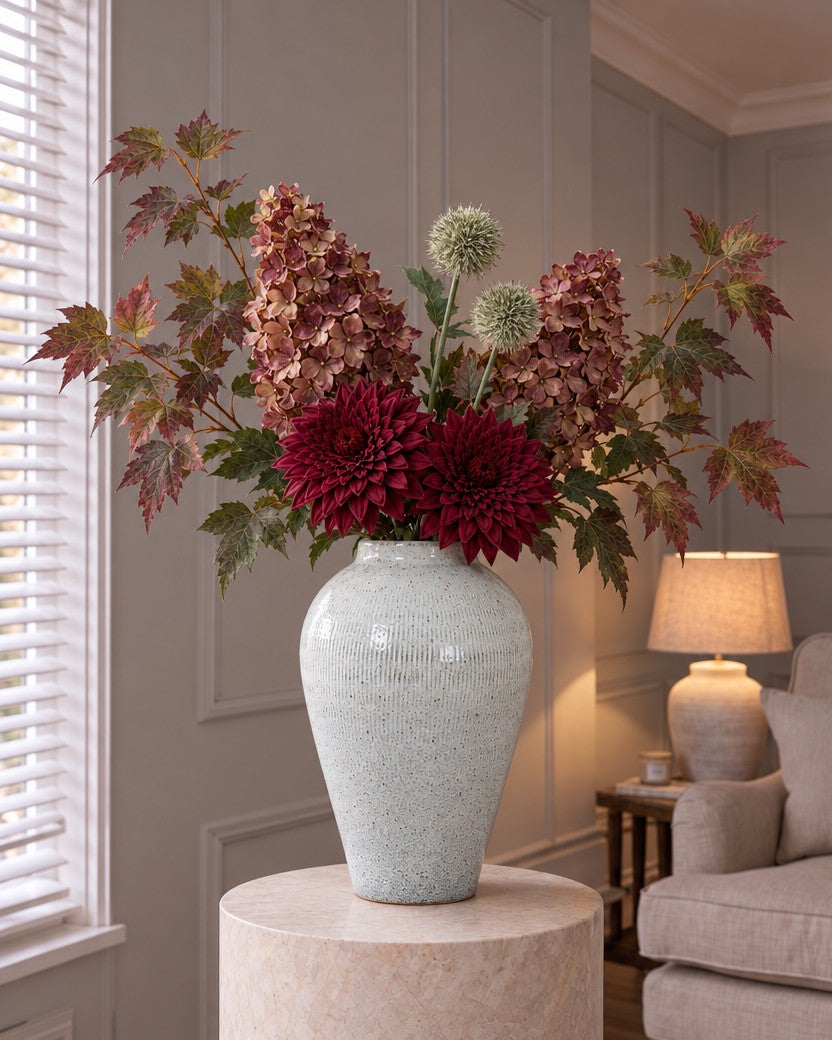 The Cotswold Manor Hydrangea & Dahlia Edit: artificial burgundy spear hydrangeas, raven dahlias at the neck, thistle globes and variegated maple in the Kemi Large Olpe Vase, on a stone plinth in a lamplit panelled living room