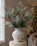 The Darcy Antique White Christmas Arrangement on a stone plinth in a panelled living room, with artificial frosted pine, burgundy rosehips, frosted cypress, silver wattle and gold sprays