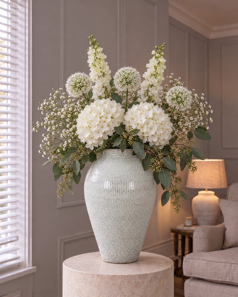The English Garden White Delphinium Classic: artificial white delphiniums, white hydrangeas, alliums, gypsophila and seeded eucalyptus in the Kemi Large Olpe Vase from the With vase option, on a stone plinth in a panelled living room