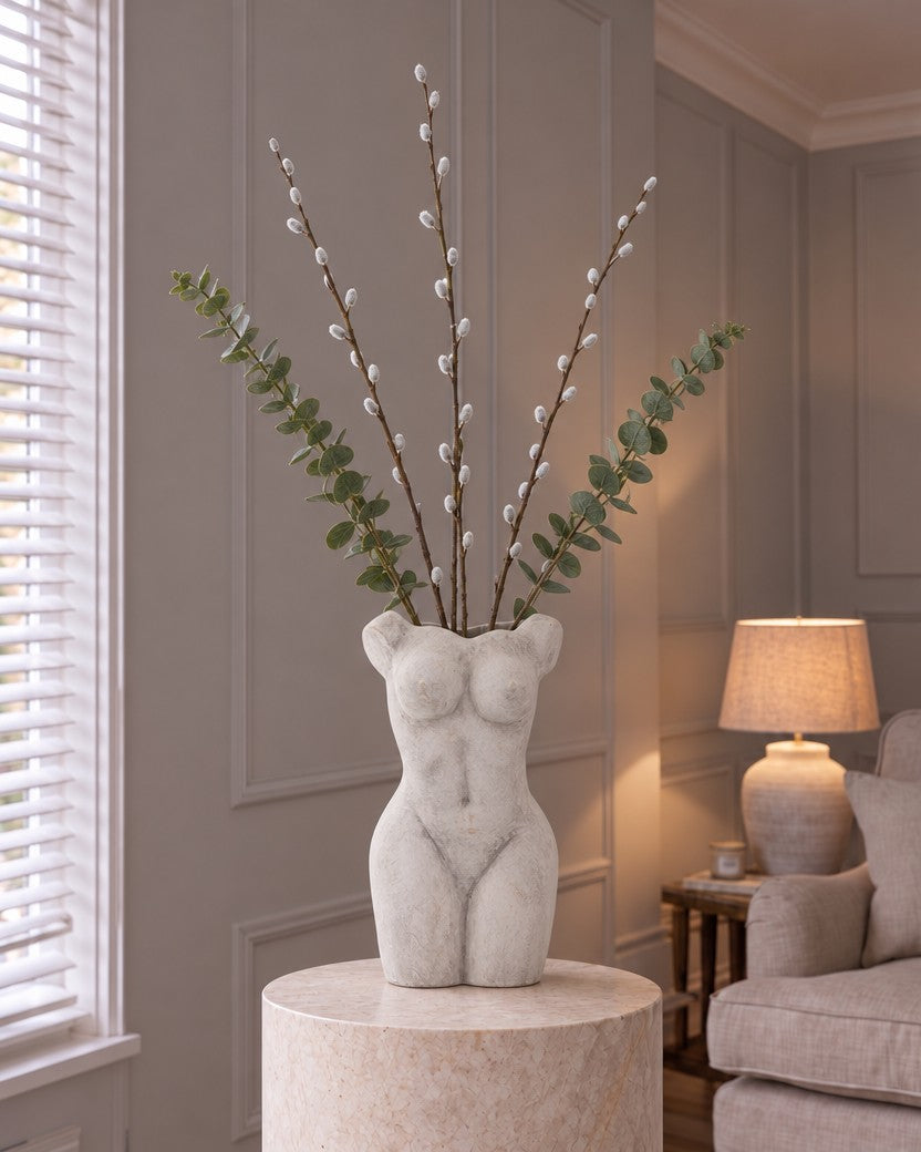 The Muse Willow Arrangement: three tall artificial pussy willow branches and two gunnii eucalyptus sprays in the stone-effect Female Figure Vase, on a stone plinth in a panelled living room