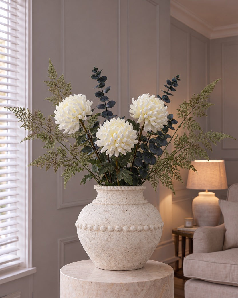 The Olympia White Arrangement: artificial white chrysanthemums, dark blue-grey eucalyptus and pale bracken fern in the Large Olympia Terracotta Vase, on a stone plinth in a panelled living room
