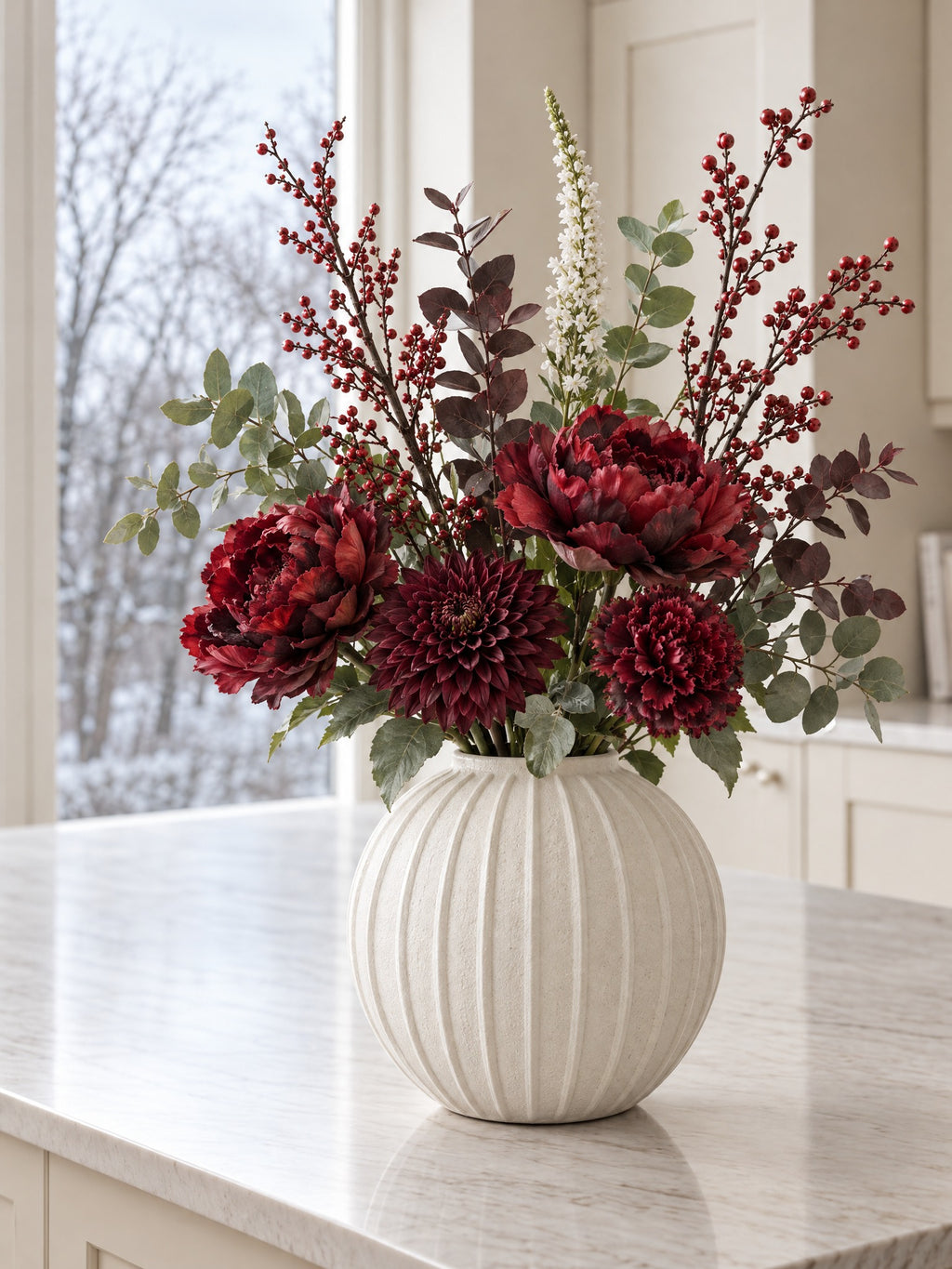 The Winter Claret Bouquet in the Grove Globe Vase, a second view: artificial burgundy peony roses, dahlia and carnation with red berry branches, eucalyptus and a white veronica spike on a marble kitchen island