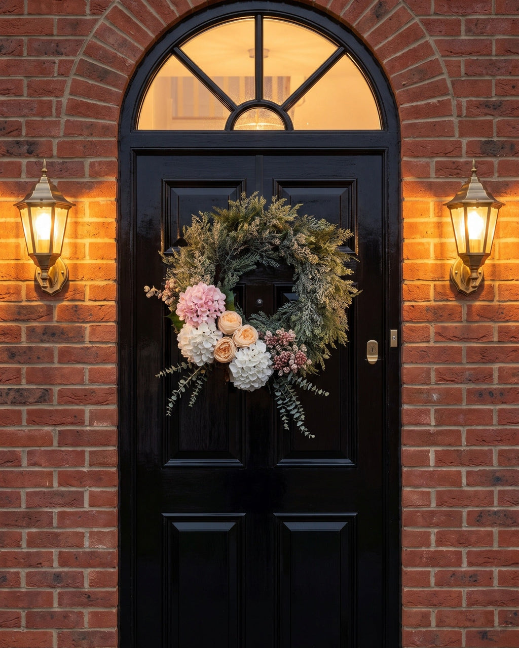 The artificial Winter Bloom Door Wreath on a black Georgian front door with lanterns at dusk